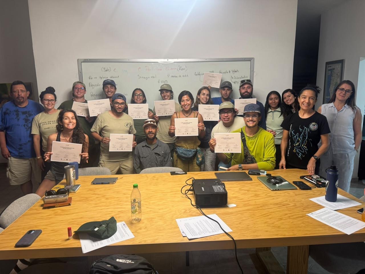 Grupo de guías sonriendo con sus constancias del curso de capacitación, frente a un pizarrón