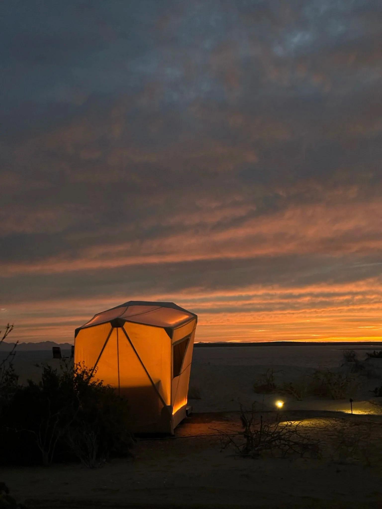 Una tienda de campaña iluminada al atardecer en el desierto