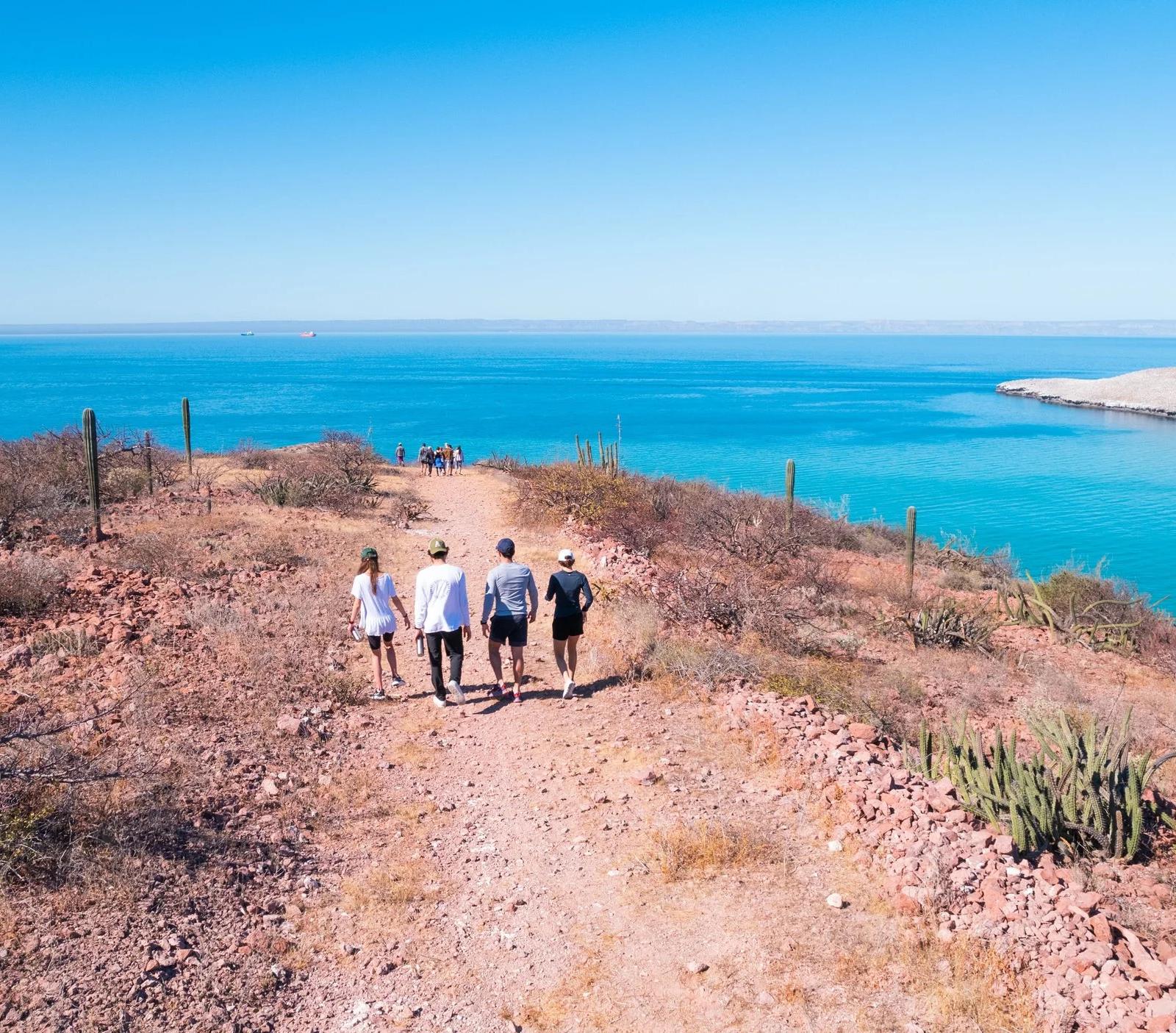 Viajeros caminando por un sendero costero sobre el agua turquesa del Golfo de California